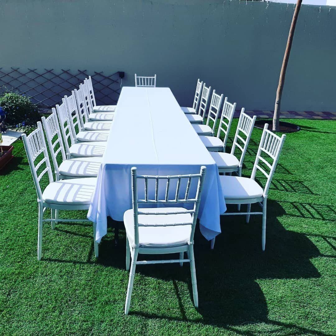 A banquet table with white chairs set on artificial grass