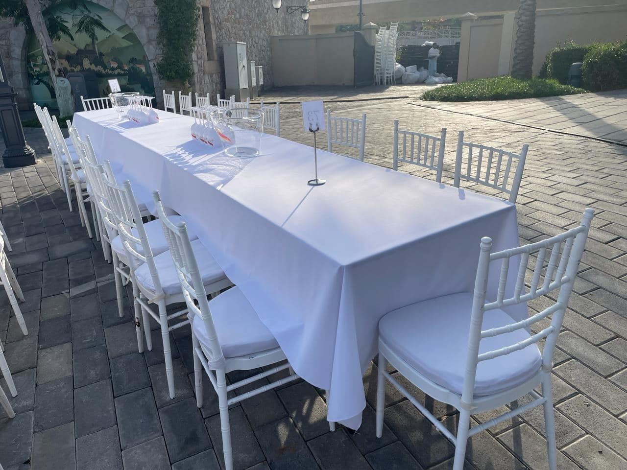 A dressed banquet table with white chairs on a paved terrace