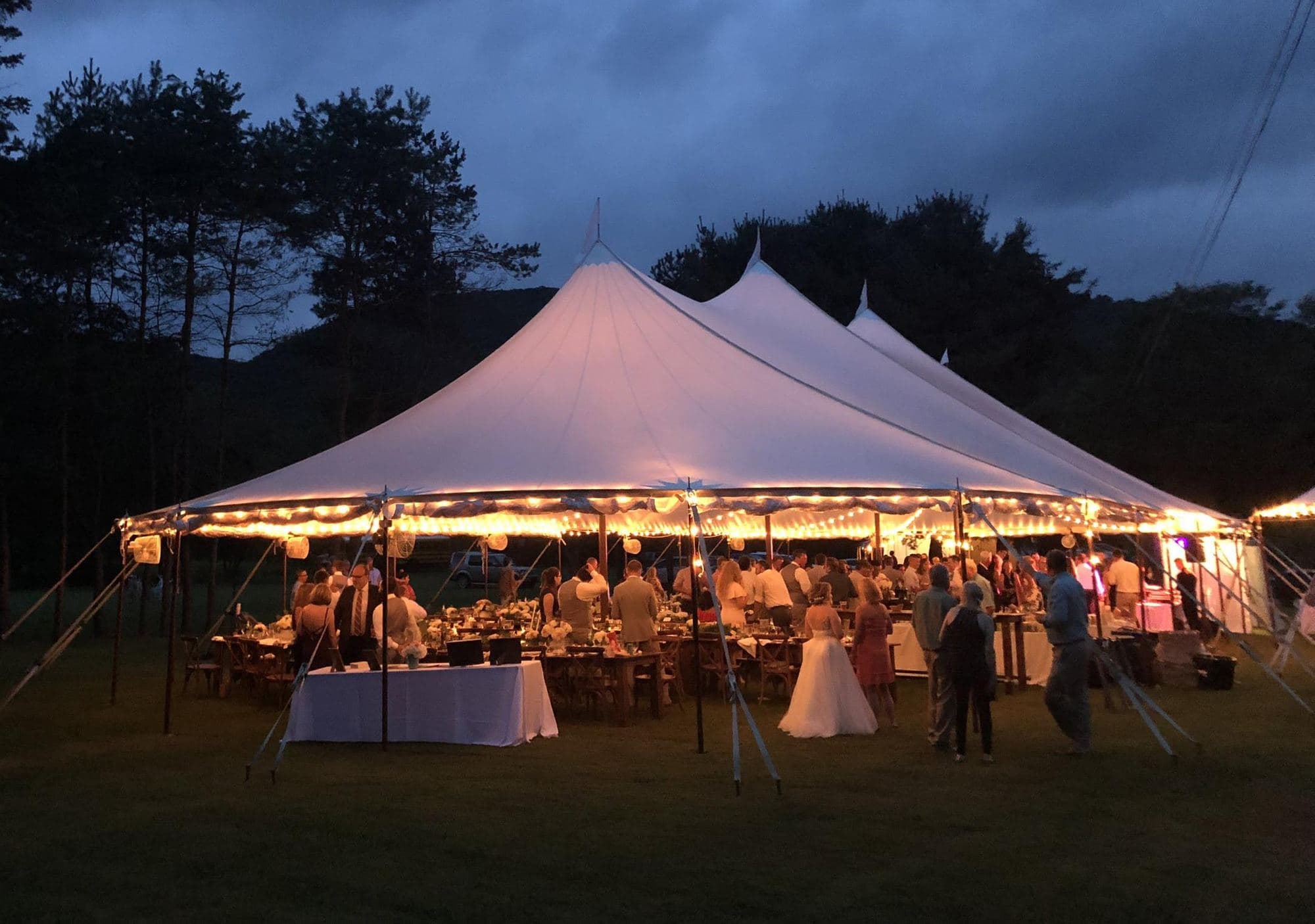 A large white peak tent lit up for an evening event